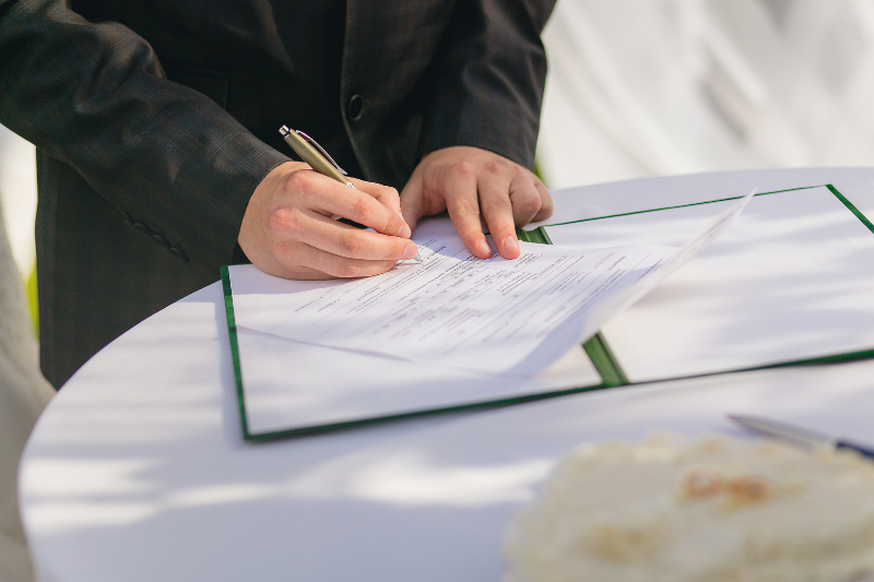 Person signing real estate license renewal paperwork at a table.