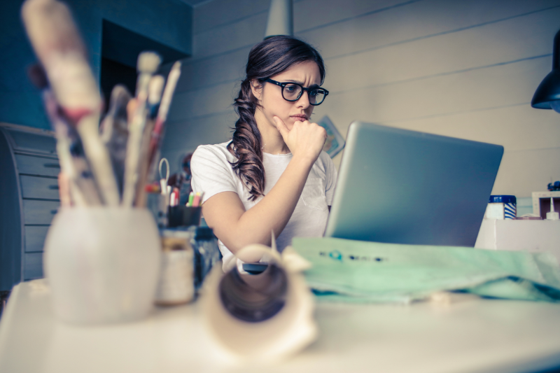 Woman thoughtfully considering a career in real estate while researching on a laptop