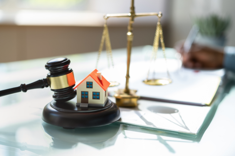 Gavel, house model, and legal scales on a desk symbolizing New Jersey real estate laws and licensing requirements for out-of-state agents.